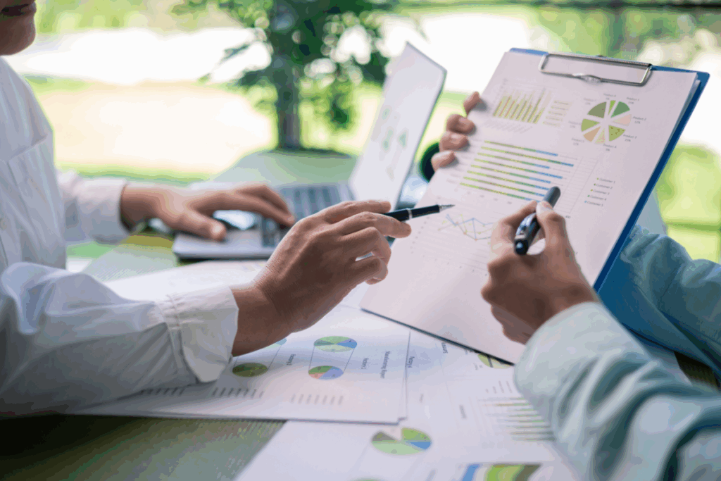 A close up of two people’s hands. They are holding and discussing sustainability reports at a table in a park.