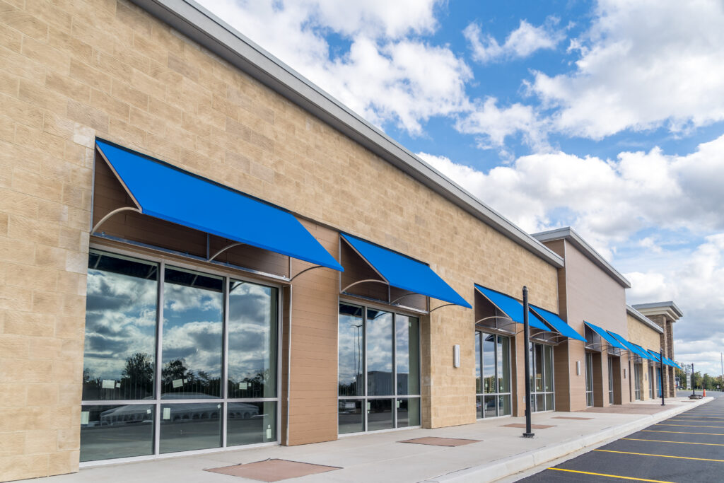 Brand new no logo, signage or label storefront of a under construction strip mall in the USA with blue awnings above the entrance, blue cloudy sky reflecting on the windows